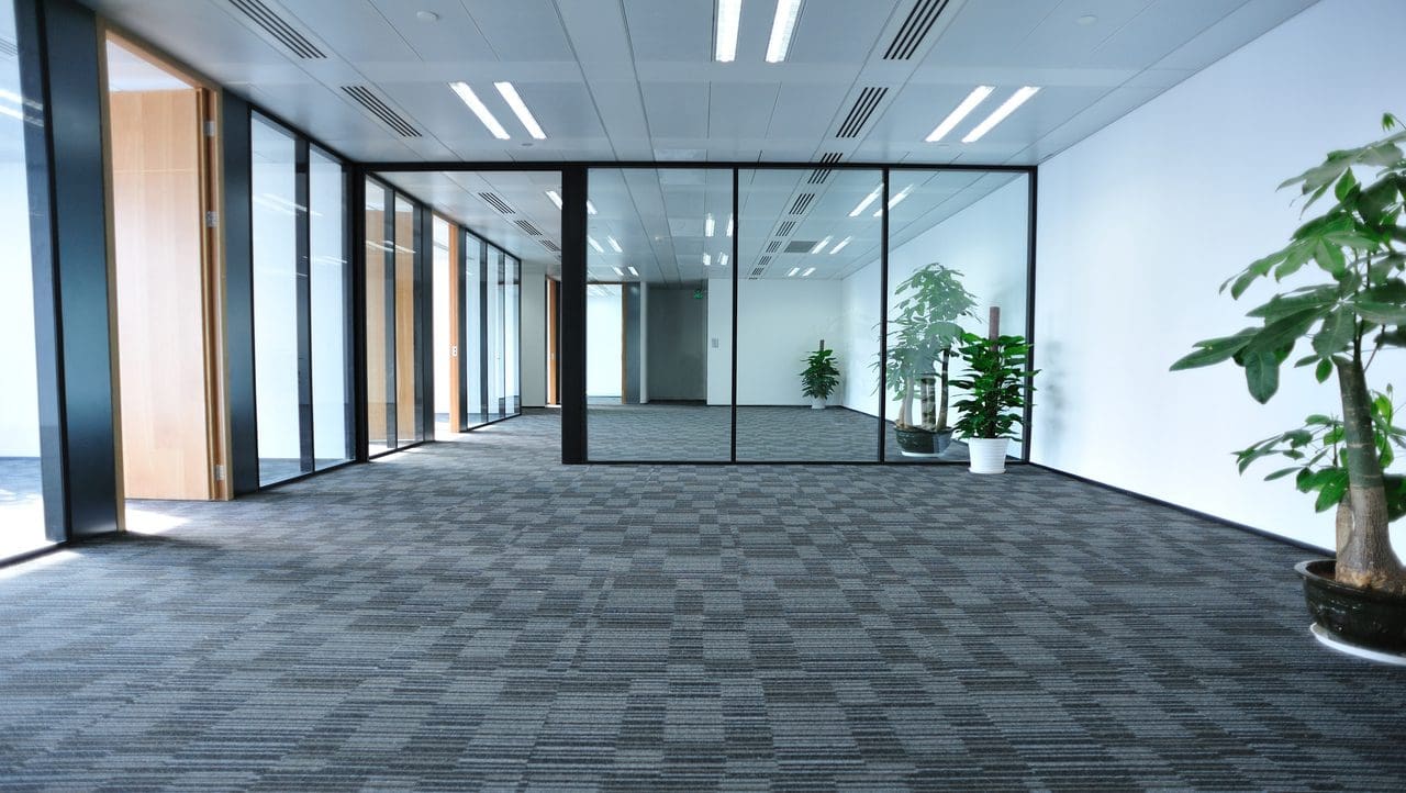 A large empty room with glass walls and plants.